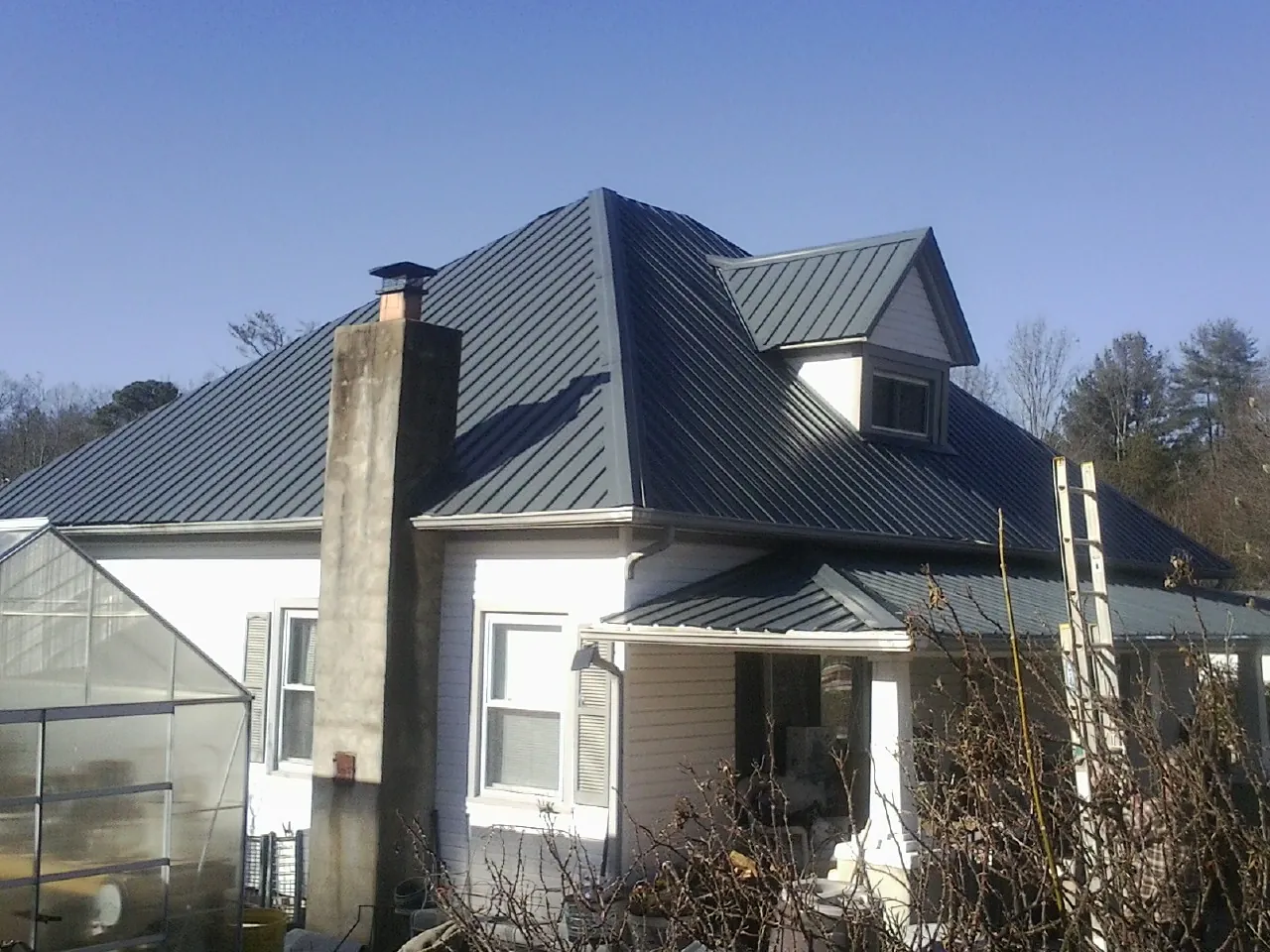 Dark blue standing seam metal roof on a white farmhouse with dormer — Slate & Tile Roof Repair by Roofing Brothers in West Wendover