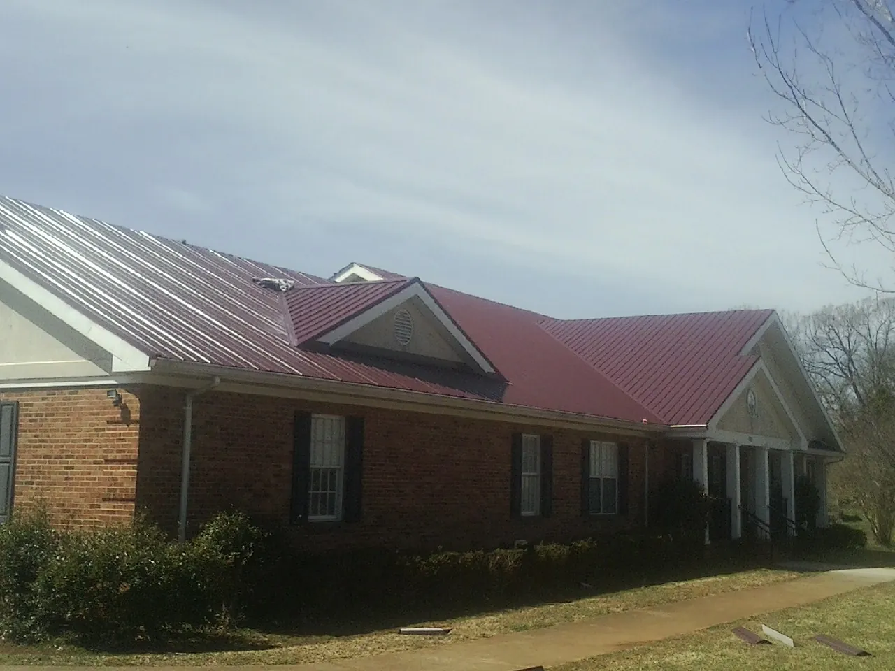 Red metal roof with gabled entries on a long brick building, from a Hail Damage Roof Repair job in West Wendover