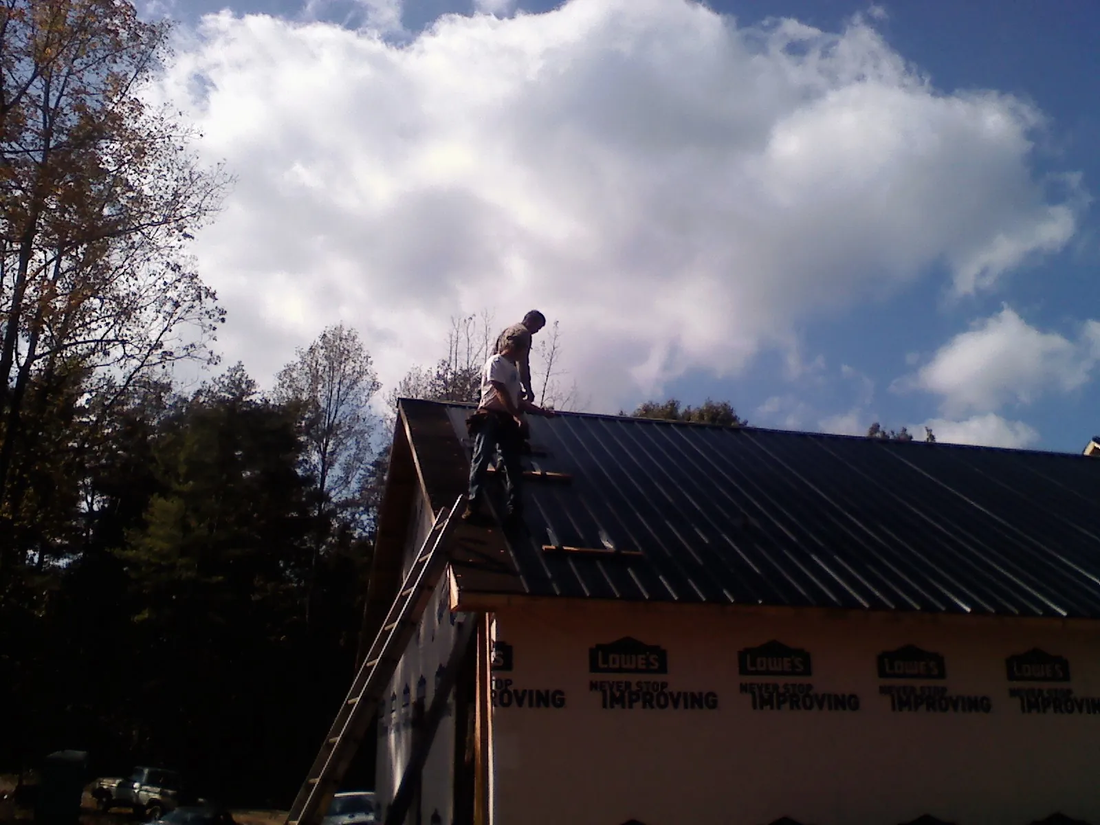 Roofer fastening dark metal panels high against a cloudy sky, from a Roof Inspection job in West Wendover